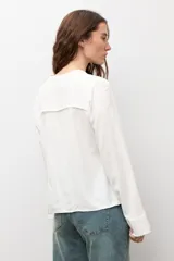 Blusa de manga larga color marrón con cuello redondo y cierre frontal con alamares. Presenta costuras visibles y diseño estructurado.