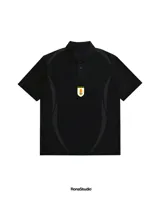 Chomba de manga corta color negro con cuello polo y cierre frontal de tres botones. Presenta un diseño minimalista con detalles tonales en los laterales y el escudo de la Asociación Uruguaya de Fútbol en 3D aplicado en el centro del pecho.