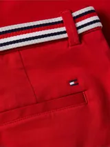 Pantalón chino rojo de corte slim, con cierre de botón y cremallera, y diseño de 4 bolsillos. Incluye un cinturón de tela a rayas blancas y azules con hebilla metálica.