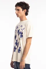 Remera de algodón color beige con estampado abstracto en azul marino y texto pequeño en el frente.