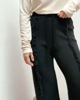 Pantalón de tejido de punto color negro, con corte recto y cintura elástica con cordón de ajuste. Presenta detalles de costuras con terminación desflecada a lo largo de las piernas.