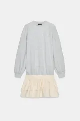 Vestido corto que combina una parte superior tipo sudadera gris de manga larga con puños, y una falda corta de volantes color crema. La parte superior es de tejido de punto jaspeado y la falda tiene dos capas de volantes.