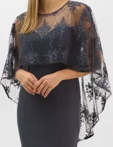 Vestido largo de corte sirena en color azul marino, confeccionado en tejido de punto con caída fluida. Presenta una capa integrada de tul fino sobre los hombros y espalda, decorada con bordados florales a tono y lentejuelas brillantes. Posee escote redondo y cierre invisible en la espalda.
