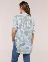 Camisa de lino sintético con estampado floral en tonos azules y beige sobre fondo blanco, de corte holgado, mangas tres cuartos y cuello camisero.