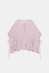 Top de cuello redondo y manga tipo capa color rosado, con detalle de tejido con textura y frunces, bajo asimétrico y cierre en espalda con botón.