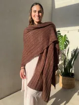 Ruana tejida en punto jersey, color negro con destellos brillantes de lurex. Presenta una etiqueta de cuero sintético con logo en la parte posterior.