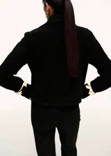 Chaqueta corta de piel bovina serraje color negro, con cuello camisero, bolsillos de parche con solapa en el frente, manga larga y cierre frontal de botones.