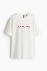 Remera blanca de algodón con corte oversized, cuello redondo y estampado frontal con texto en color rojo.