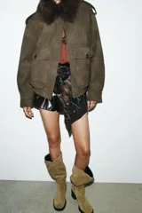 Cazadora color verde militar con efecto ante, cuello solapa con aplicación de pelo sintético desmontable, manga larga con puño, trabillas en los hombros y bolsillos frontales con solapa y botón. Cierre frontal con cremallera y botones ocultos.