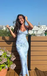 Vestido largo ajustado, color celeste claro, con estampado floral en tonos de azul. Presenta escote drapeado con tirantes finos ajustables.