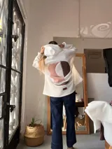 Campera con capucha confeccionada en tejido tipo corderito blanco, con diseño de collage abstracto en la espalda en tonos rosado y marrón. Presenta un corte holgado y una etiqueta de cuero sintético en la parte inferior.