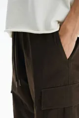 Pantalón cargo slim fit marrón, con cintura elástica ajustable mediante cordón, bolsillos laterales con solapa y costuras decorativas en las rodillas.