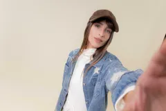 Camisa de denim de lavado medio, con calce relajado y ligeramente oversize. Presenta bordados o estampados de inspiración celestial (soles, lunas y estrellas) en color claro en la parte delantera y mangas. Tiene cuello, bolsillos delanteros con tapa y cierre frontal con botones.