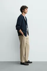 Pantalón de corte recto confeccionado en tejido elástico, con cintura elástica, pliegues frontales, bolsillos laterales y bolsillos traseros de vivo con botón.