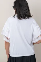 Remera de algodón color blanco, con cuello redondo y mangas cortas holgadas que presentan detalles de encaje broderie.