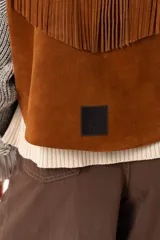 Chaleco oversize confeccionado en cuero descarne, con diseño de terminación en picos, detalle de tachas metálicas en los bordes frontales y flecos en la espalda.