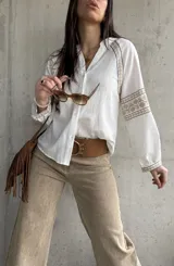 Camisa blanca de calce relajado y tejido liviano, con escote en V y delicados detalles bordados geométricos en tonos tostados en las mangas abullonadas y puños.
