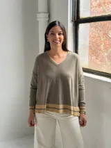 Sweater de punto en color verde oliva, con cuello en V y diseño holgado. Presenta detalles de franjas en color beige en el cuello, los puños y el ruedo.