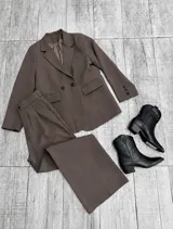Conjunto sastrero de dos piezas color marrón chocolate, compuesto por un blazer oversize de doble botonadura con solapas y bolsillos con solapa, y un pantalón largo de corte recto con pinzas en la cintura.