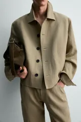 Sobrecamisa cropped fit de lino color beige, con cuello solapa, mangas largas con puño abotonado, bolsillos frontales de vivo y cierre frontal con botones oscuros.