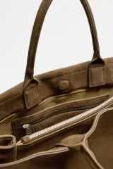 Bolso de mano extragrande color marrón oscuro, estilo tote o satchel, fabricado en piel. Presenta dos asas de mano y un detalle de cinta ajustable con cierre de solapa en la parte frontal superior.