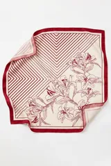 Pañuelo cuadrado con diseño dividido en dos secciones: una con estampado de líneas geométricas en ángulo y otra con ilustración botánica de flores tipo lirios en trazo negro sobre fondo crema. Presenta un borde perimetral en color negro.