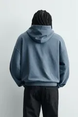 Sudadera tipo hoodie de corte relajado en color azul con efecto lavado. Presenta capucha, mangas largas, puños y ruedo en rib, con estampado frontal en color blanco con texto y números.