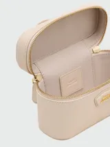 Cartera tipo vanity bag de Marc Jacobs, color beige, con cierre superior, asa corta superior y correa larga ajustable y extraíble. Presenta logo metálico dorado en el frente.