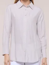 Camisa de calce relajado color celeste, confeccionada en tejido de textura suave y fluida. Presenta cuello camisero y abotonadura frontal, mangas largas con puño ancho y ruedo curvo.