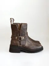 Bota corta de cuero vacuno en color chocolate con efecto desgastado. Presenta una suela track de goma negra, detalle de pulsera desmontable con tachas metálicas y cierre lateral.