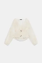 Blusa de escote en pico y manga larga con puños elásticos. Presenta un diseño semitransparente con bordados florales a tono, cintura elástica y cierre frontal mediante lazos con abalorios decorativos.