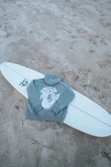 Hoodie gris con capucha y cordones ajustables, de corte holgado y puños elásticos. Estampado en la espalda con una sirena, una flor de hibisco y la frase "Glass Waves".