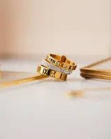 Anillo triple dorado de acero quirúrgico con baño de oro 18k. Dos de los anillos tienen números romanos grabados y el anillo central tiene circonitas blancas.