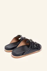 Sandalias de cuero color negro con dos tiras anchas sobre el empeine, cada una con hebillas metálicas ajustables y detalles de tachas plateadas. La suela es de cuero con un borde de color madera.