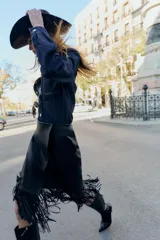 Falda midi negra con efecto piel, diseño cruzado en el delantero y flecos en el bajo. Cierre lateral con cremallera oculta.