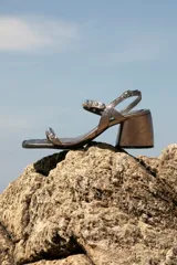 Sandalia de cuero color bronce metalizado, con punta cuadrada, taco ancho y bajo, y tiras finas adornadas con tachas esféricas plateadas.