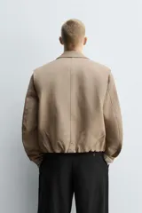 Cazadora de corte cropped confeccionada en tejido de algodón con interior ligeramente acolchado. Presenta cuello solapa, manga larga, bolsillos de vivo en la cadera y bajo ajustable con cordón. Cierre frontal mediante cremallera oculta por solapa con botones a presión.