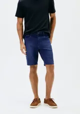 Bermuda de jean azul oscuro, de corte clásico con cinco bolsillos, cierre frontal y pasacintos.