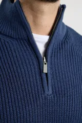 Sweater verde de punto inglés con cuello alto y cierre metálico frontal. Tiene mangas largas y terminaciones en punto canalé.