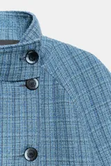 Chaqueta corta de cuello subido y manga larga, con diseño de cuadros en tonos azules. Presenta cierre frontal cruzado con botones oscuros y bolsillos de vivo en el delantero.