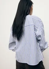 Camisa crop de corte recto confeccionada en mezcla de algodón, poliéster y viscosa. Presenta diseño de rayas verticales en azul y blanco, cuello camisero, bolsillo aplicado en el pecho y cierre delantero con botones.