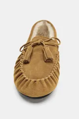Mocasín de mujer confeccionado en serraje color tostado, con detalle de fruncido y borlas en la parte delantera. Presenta un interior forrado en tejido efecto borreguito y suela plana.