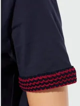 Remera Moncler de algodón azul marino con cuello redondo y manga corta. Presenta puños tejidos con patrón en zigzag rojo y azul marino, y un parche rectangular rojo con el logo de la marca en el borde inferior.