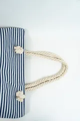 Bolso de tela tipo tote bag con estampado de rayas horizontales azules y blancas, y base de color beige. Tiene asas de cuerda de color beige.