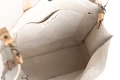 Bolso tipo tote de cuero con acabado texturizado en tono blanco desgastado. Cuenta con doble asa de mano y una correa larga ajustable y extraíble en color tostado. Presenta un bolsillo frontal externo y herrajes metálicos.