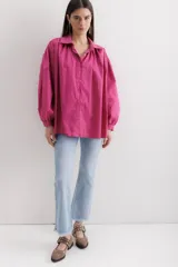 Camisa fucsia de algodón, corte holgado, con cuello camisero, cierre frontal con botones y mangas largas abullonadas con puños abotonados.