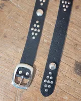 Cinto de cuero marrón con hebilla metálica de estilo envejecido y detalle de tachas metálicas en diferentes tonos en el extremo.