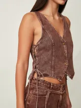 Top estilo chaleco crop de denim marrón con efecto acid wash, escote en V, cierre frontal con botones metálicos y cordones ajustables en los laterales.