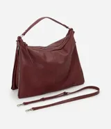 Bolso tipo hobo de gran tamaño en color bordó, confeccionado en poliuretano. Presenta una estructura desestructurada, cierre superior, correas dobles (una de mano y una larga desmontable) y cierres laterales decorativos con tiradores.