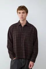 Camisa de corte boxy confeccionada en franela a cuadros, con cuello clásico, cierre frontal de botones, bolsillo en el pecho y puños abotonados.